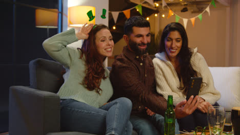 Group-Of-Friends-Dressing-Up-At-Home-Or-In-Bar-Celebrating-At-St-Patrick's-Day-Party-Posing-For-Selfie-On-Phone